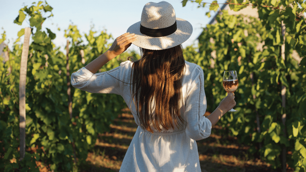 Lady walking through vineyard with a glass of rosé wine